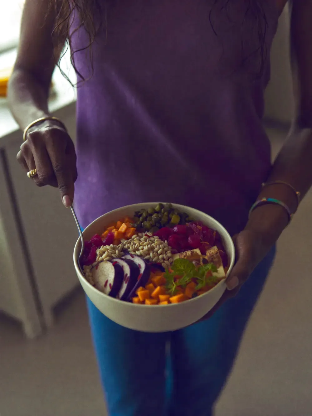 A colourful, balanced grain bowl being plated in a bright kitchen